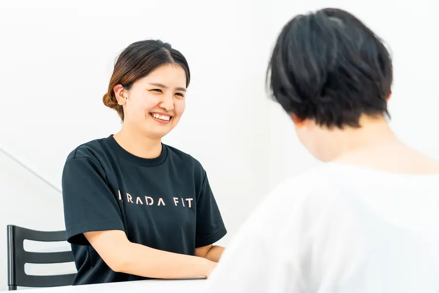 指導風景:向かい合って座り、女性の話を笑顔で聞くコーチ