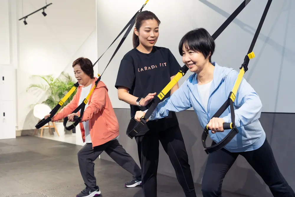指導風景:ストラップを使って運動する女性たちと、隣で動きを見るコーチ